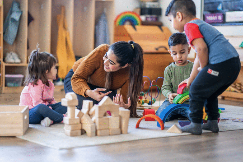Eine Erzieherin ist auf dem Bauteppich in der Interaktion mit drei Kindern. Das Foto ist von Canva Pro (FatCamera) 