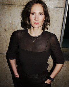 Miriam Haberer-Zeleke steht in einem schwarzen Meshoberteil vor einer Wand, sie hat die Hände locker in den Hosentaschen und schaut in die Kamera. ihre kurzen Haare trägt sie offen.