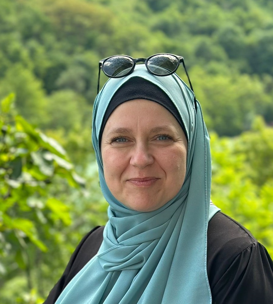 Dr. Dres. Agata Skalska steht im Grünen und lächelt in die Kamera. Sie trägt einen türkisenen Hidschab und hat eine schwarze Sonnenbrille darauf gesteckt.